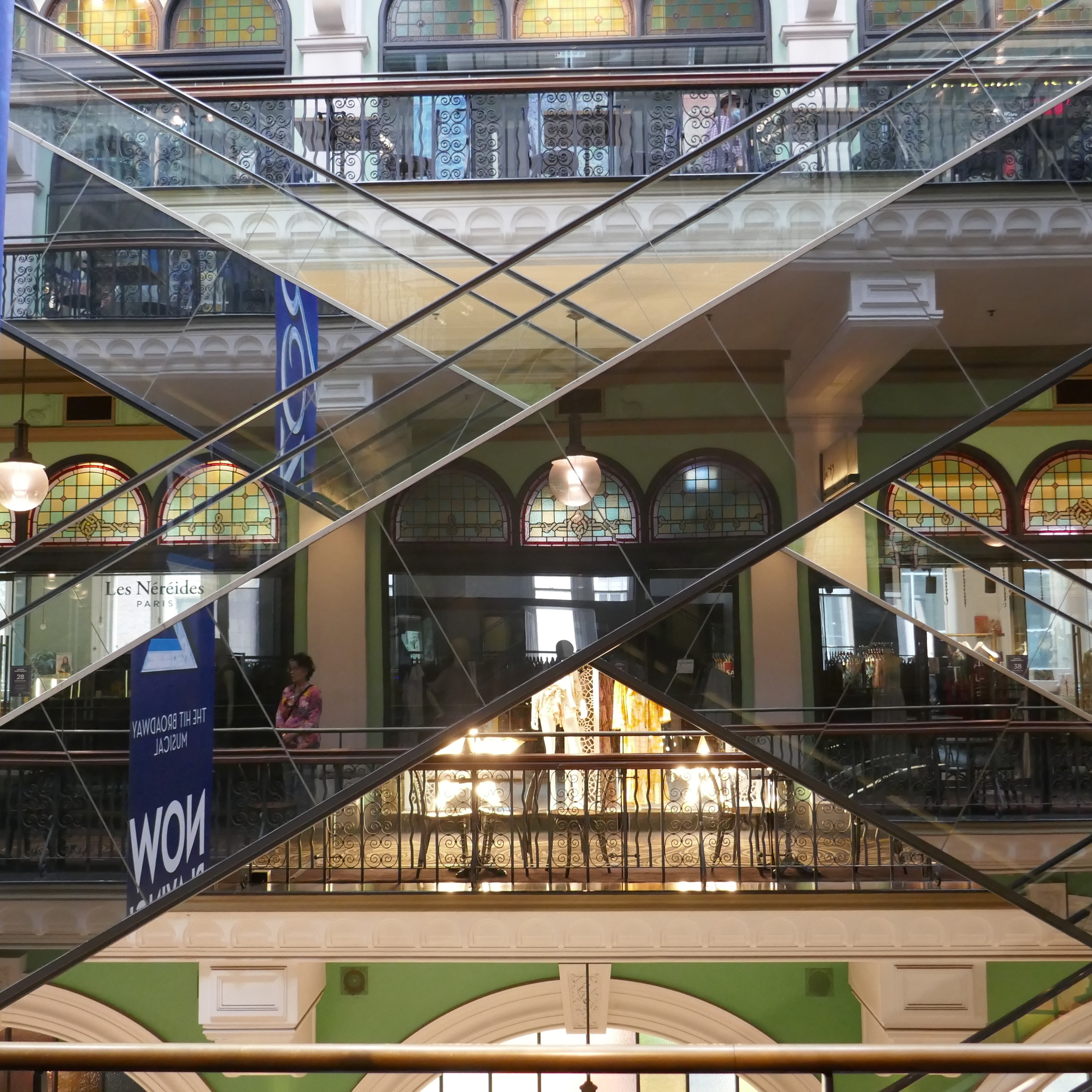 a scene from inside Sydney's Queen Victoria Building, with escalators forming a diagonal cross, while showing reflections of the shops behind the photographer