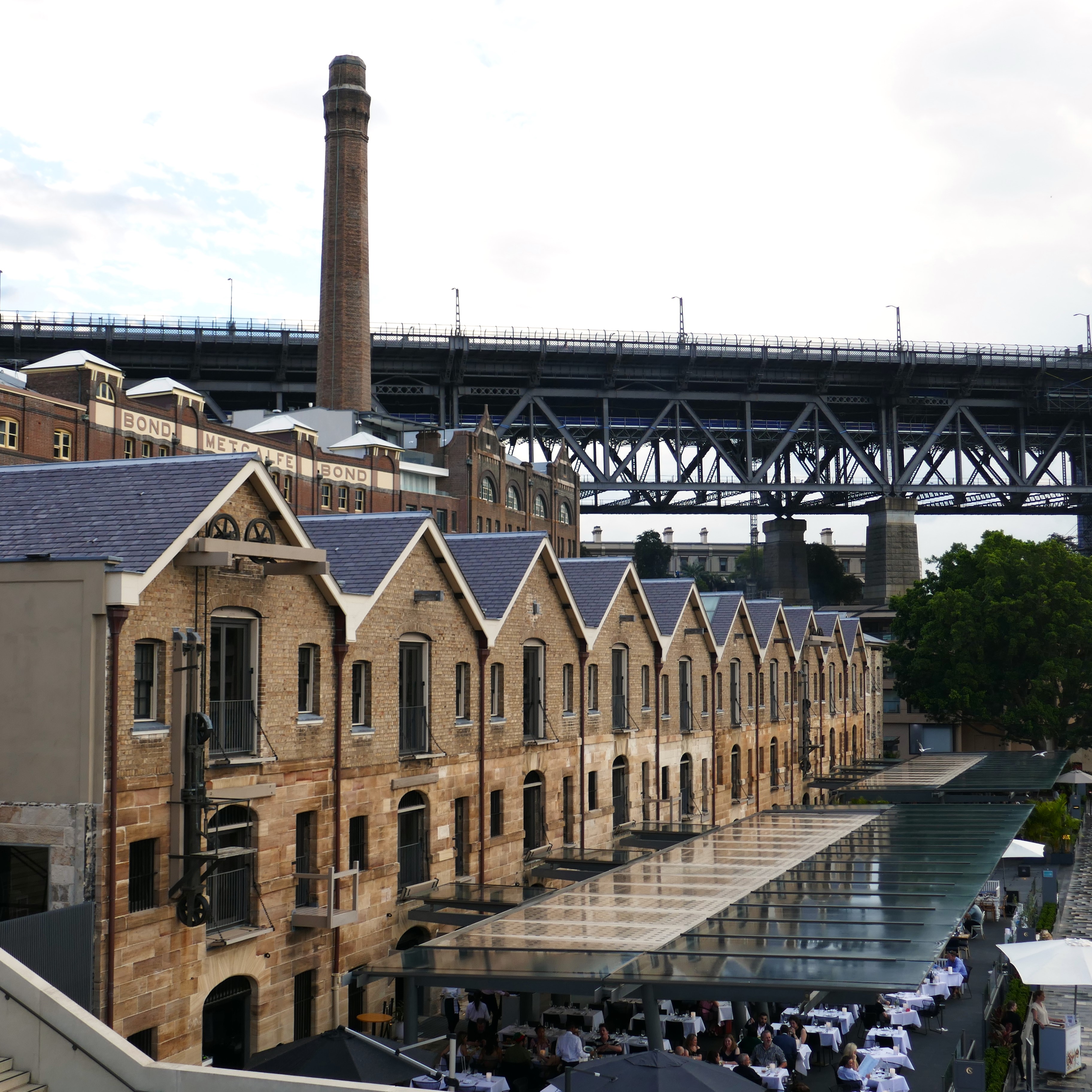 A view along the front of Campbell's Stores, on the edge of Sydney Cove, with the chimney of the former power station (and Mining Museum) in the background 