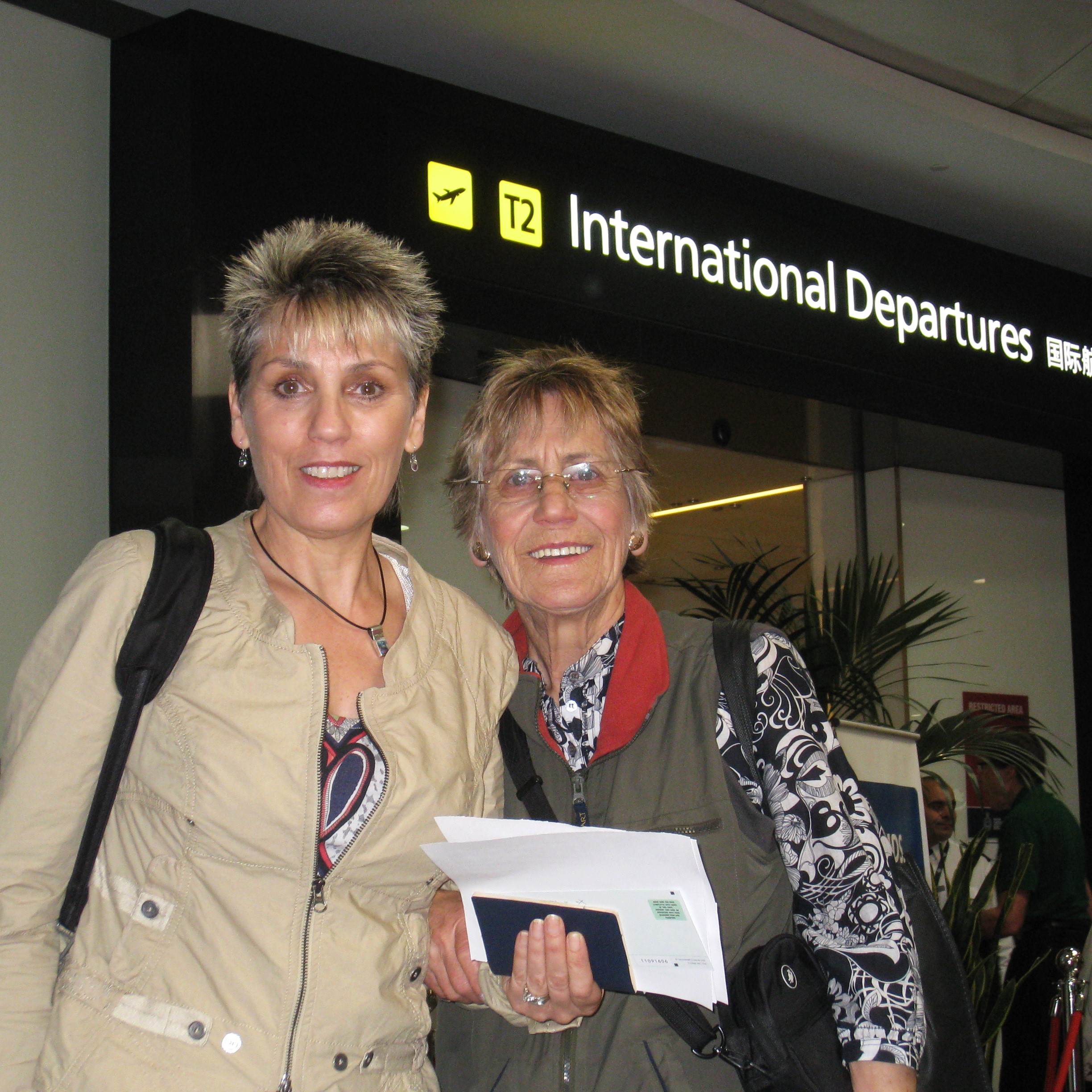 Two passengers at the International Departures gate, one holding a passport and other documents for border officials to process