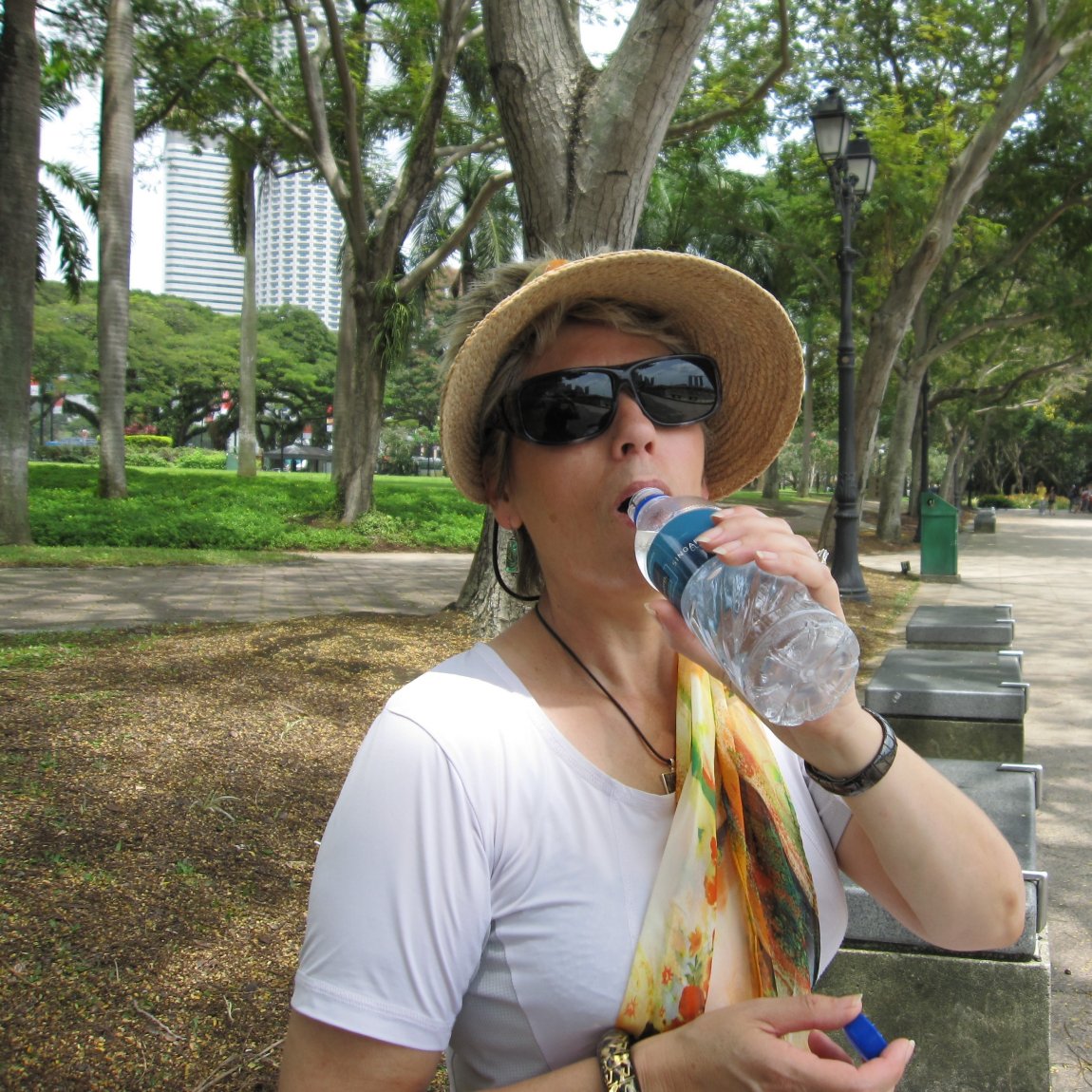 Image of a walker taking a drink from a plastic bottle, with a background of tropical trees 