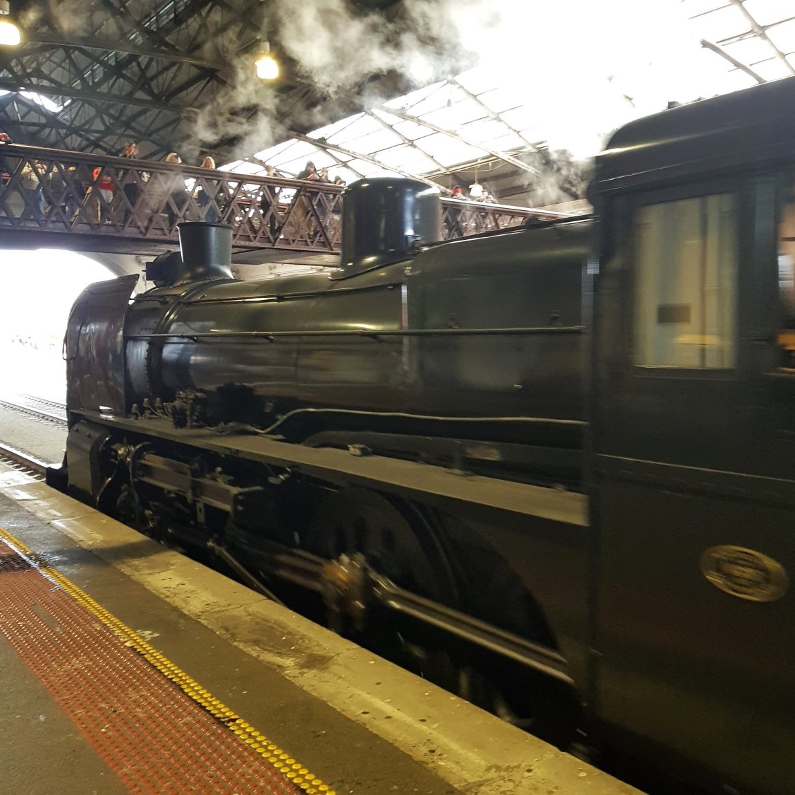 An image of Steamrail A2 986 abouot to pass under the Ballarat Station Overhead Bridge, with people watching fromn on the bridge