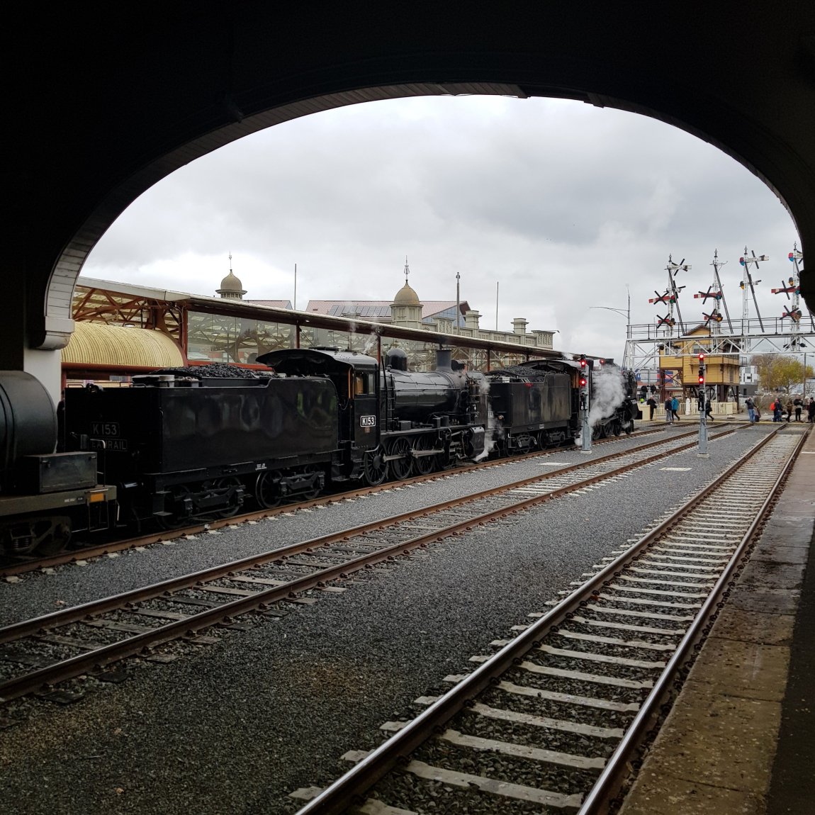 An image of Steamrail Steam engines K15 and A2 986 stoped outside the Ballarat Great Train Hall, with the restored heritage Semaphore Signals in the background