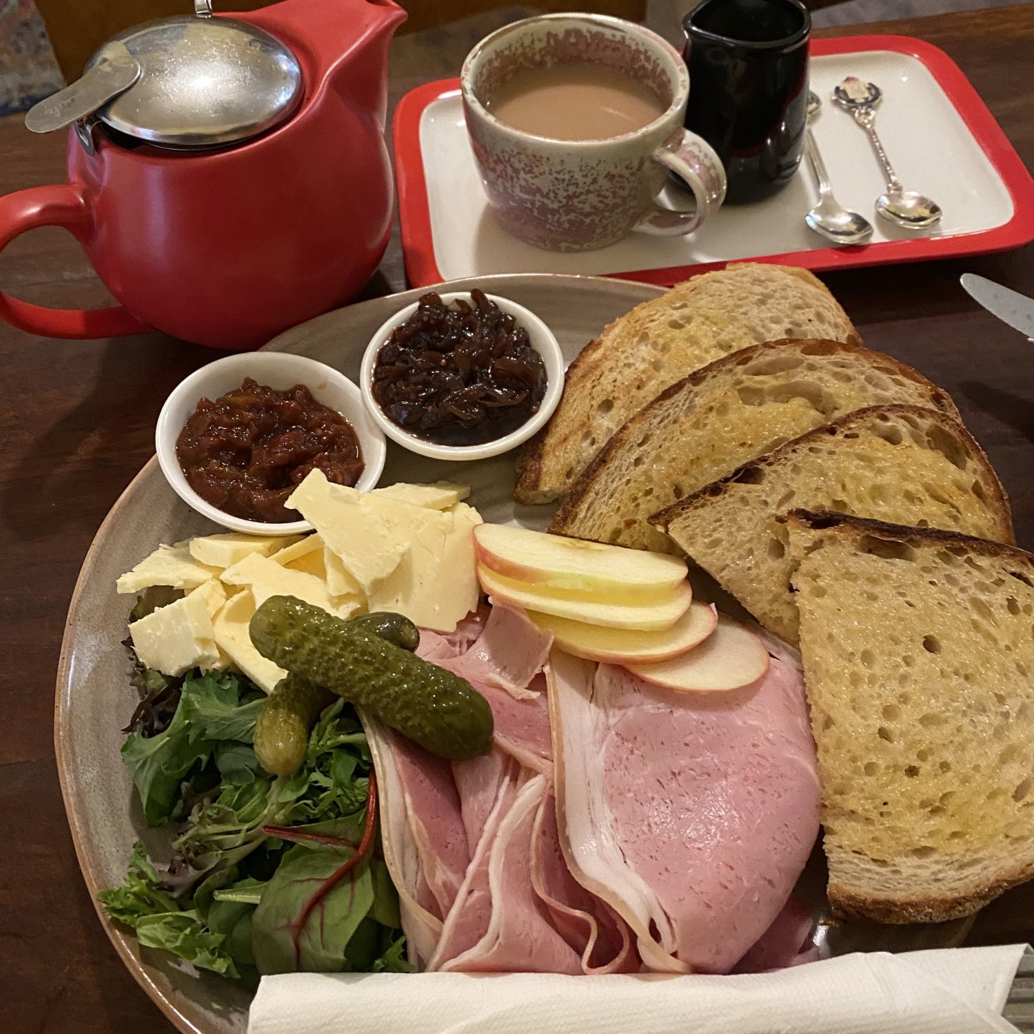 image shows a plate with bread, sliced apple, sliced ham, cheese, pickles, etc.