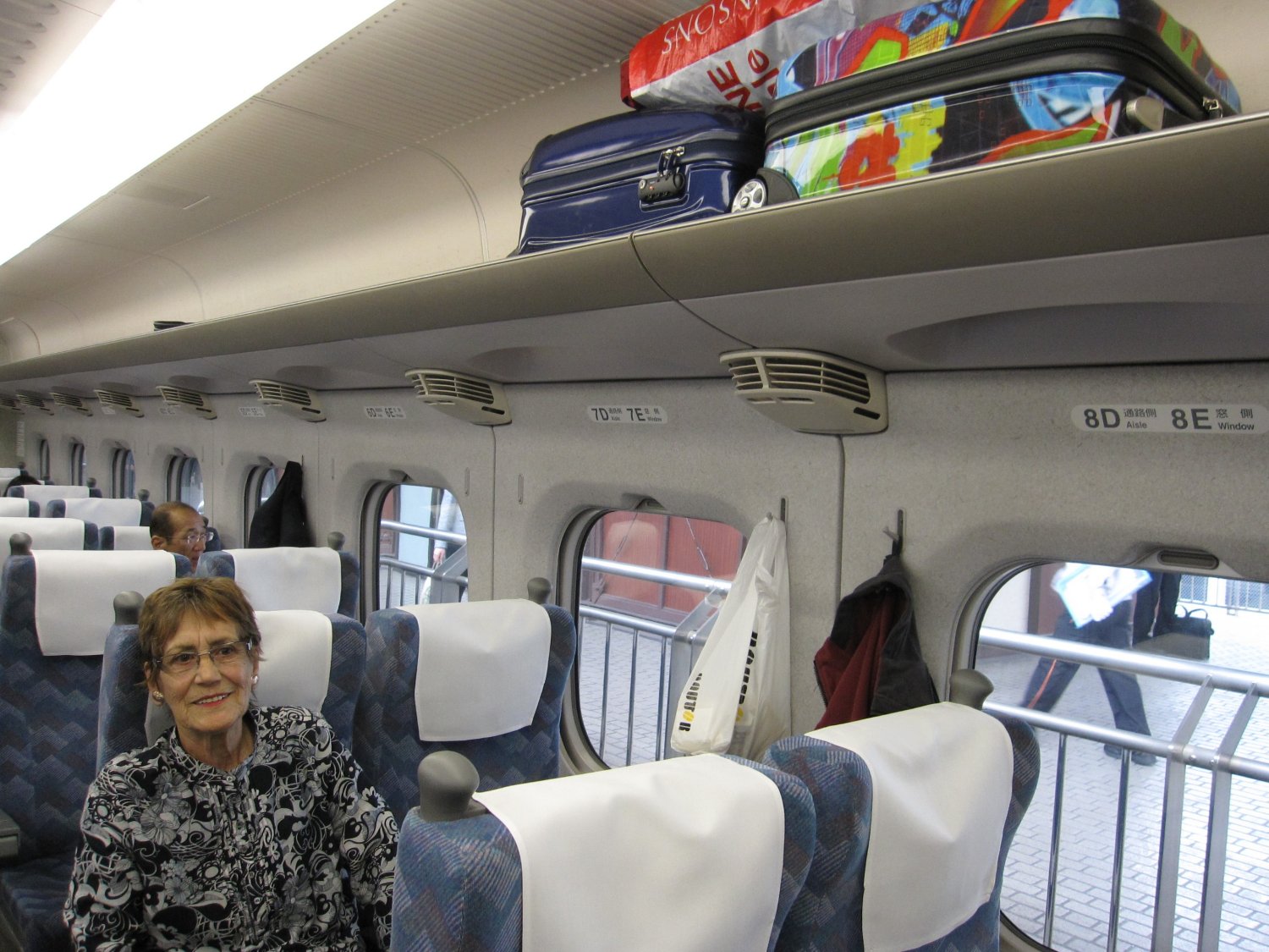 image of a Shinkansen bullet train cabin, with a passenger sitting below several bags in the overhead rack