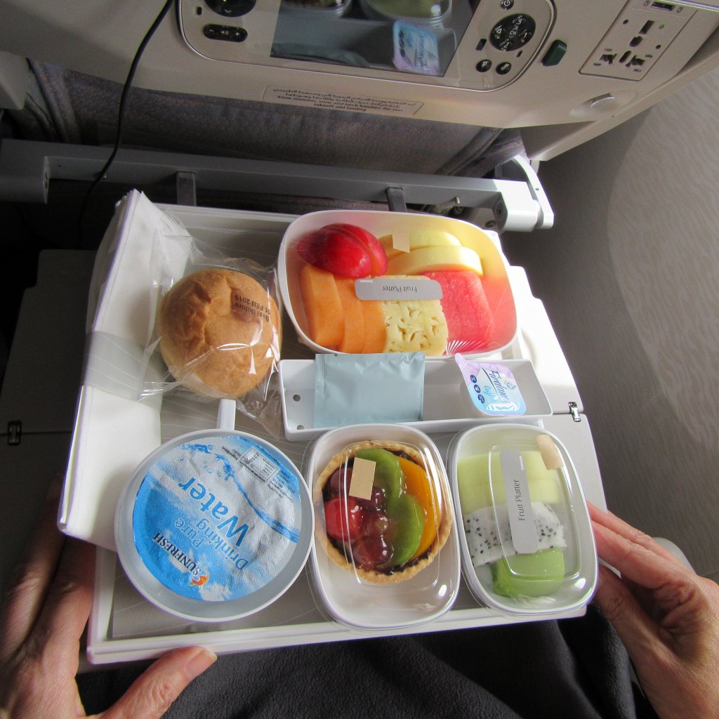 Image of an inflight fruit platter - showing three containers of fruit, a small container of water, and a fresh bun