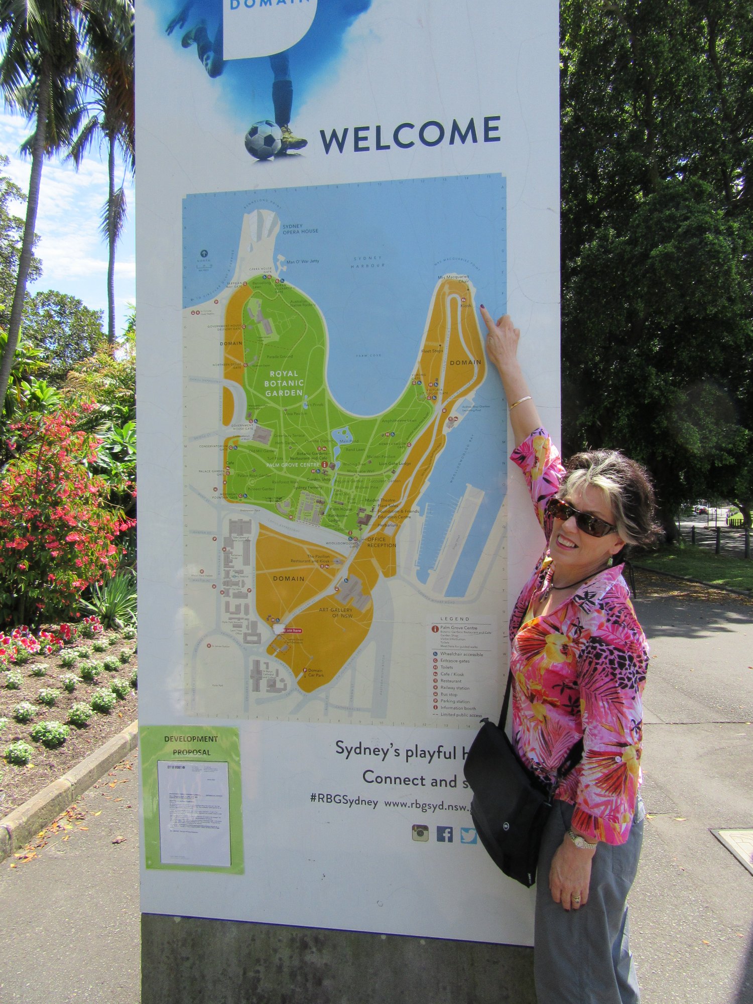 image of Marlene standing beside a map board showing the Sydney Royal Botanic Garden, pointing to Mrs Macquarie's Chair
