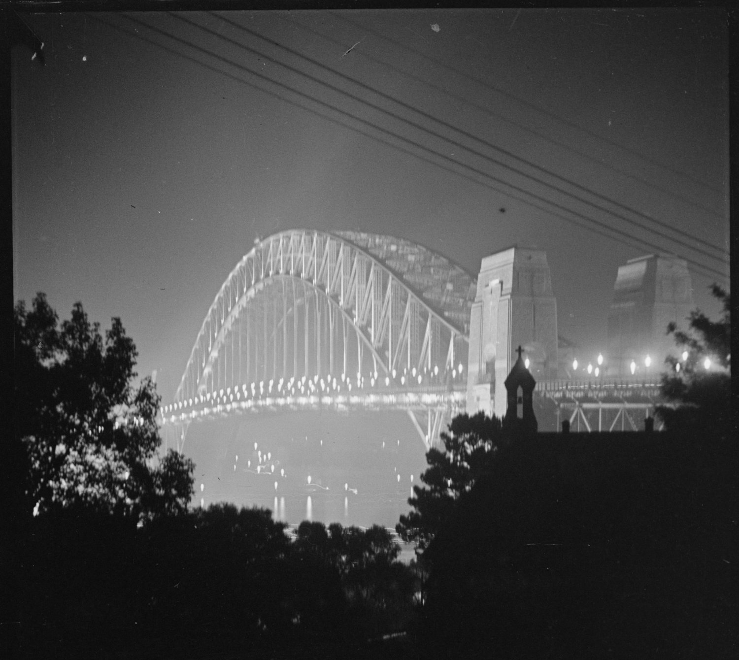 image showing a night view of an illuminated Sydney Harbour Bridge from Upper Pitt Street, Kirribilli, taken in 1938. Credit: City of Sydney Archives