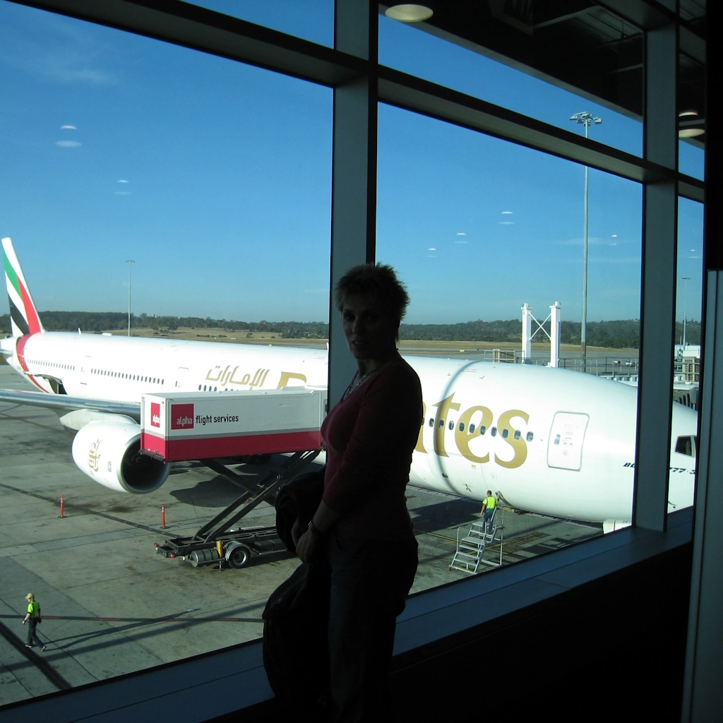 Image of a traveller stanind in from of an airport departure lounge window, with an Emirates airliner visible in the background