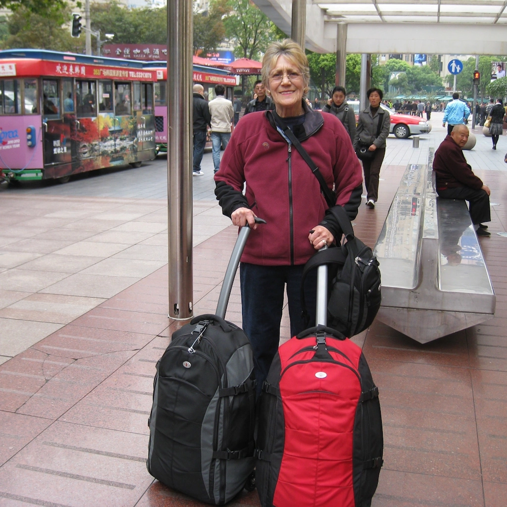 Image of Marlene's Mum, with two travel bags at a transit point in China